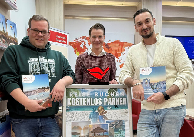 Drei Personen, die jeweils eine Broschüre in der Hand halten, stehen vor einer Landkarte und einem Schild für "Reise Buchen Kostenlos Parken", einem Reisebüro in Deutschland.