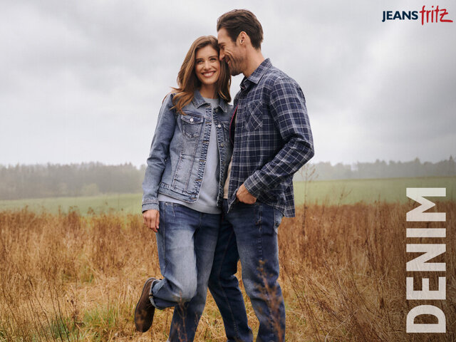 Ein Paar, gekleidet in Jeans und Karohemden, steht in einem Feld mit hohem Gras, im Vordergrund ist das Wort „DENIM“ zu sehen, über ihnen ein bewölkter Himmel.